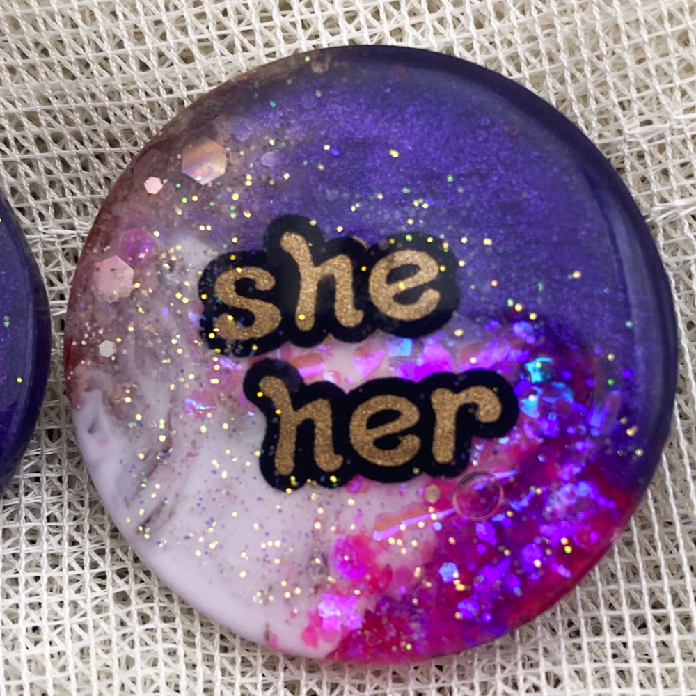 Purple, pink, white and gold statement pronoun badge with  she/her label