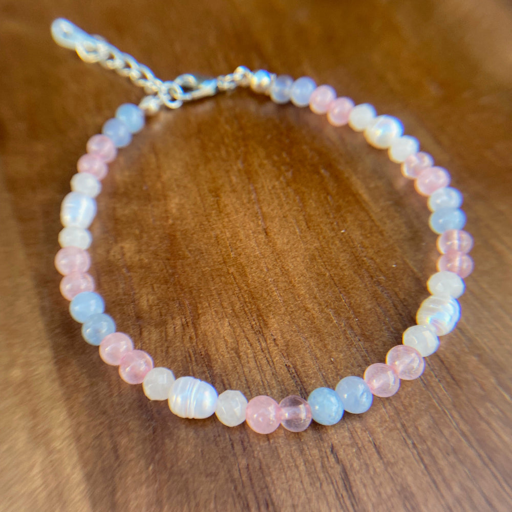 Beaded bracelet in pale pink, light blue and translucent white stone beads in a gradient resembling the trans pride flag