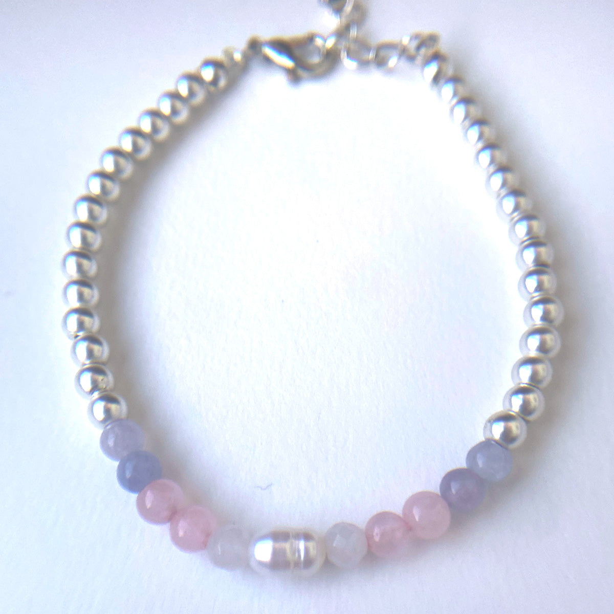 Top down view of silvery beaded bracelet with a panel of in pale pink, light blue and white and pearl beads resembling the trans pride flag