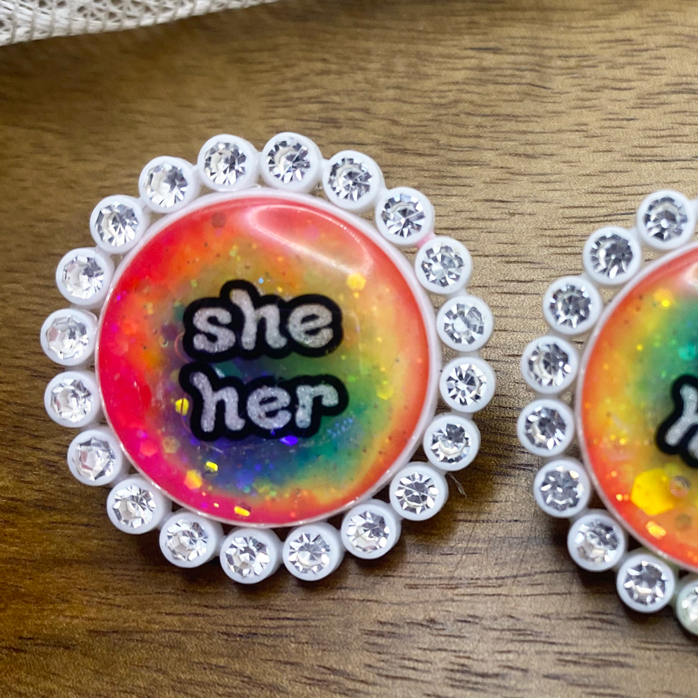 White rhinestone glowing rainbow pronoun pin with she/her label