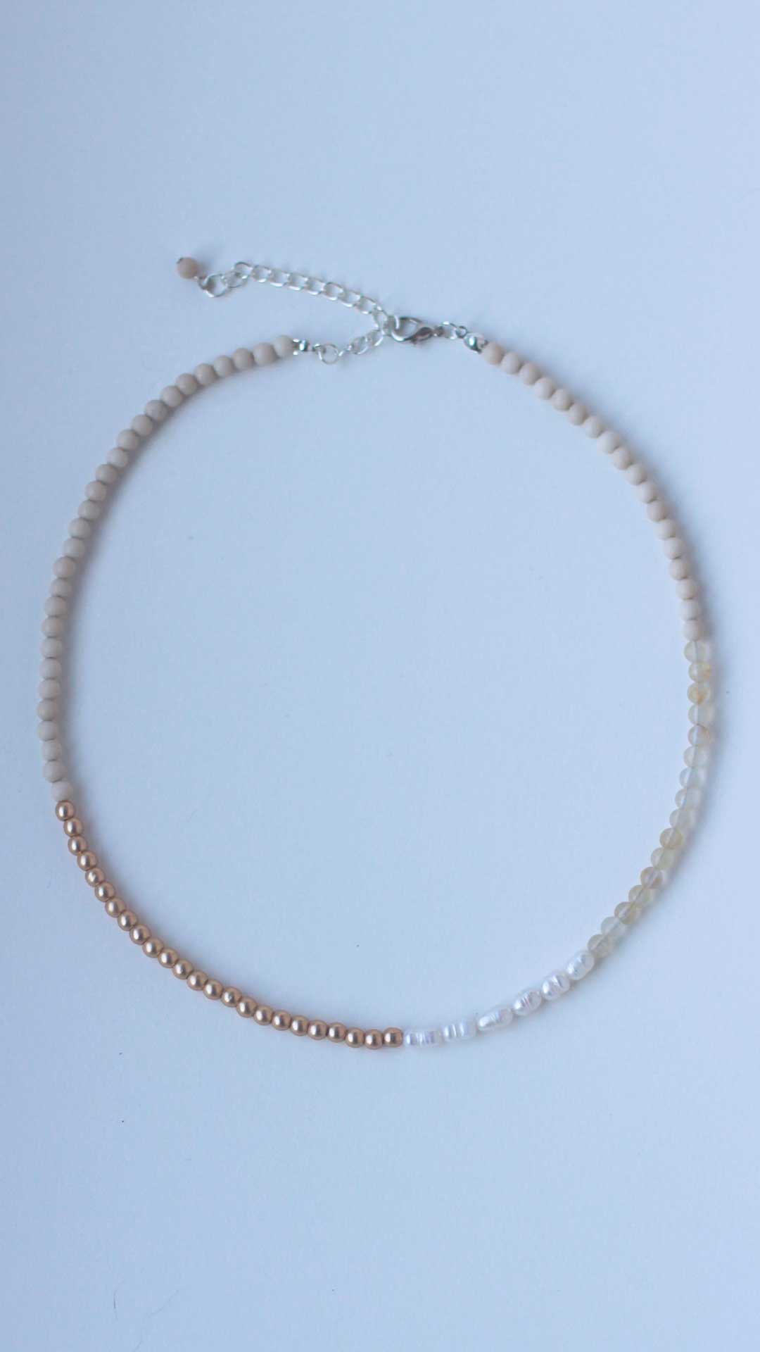 Top down view of a gender neutral necklace featuring freshwater pearls and fossil, citrine and gold-coated hematite 4mm natural stone beads 