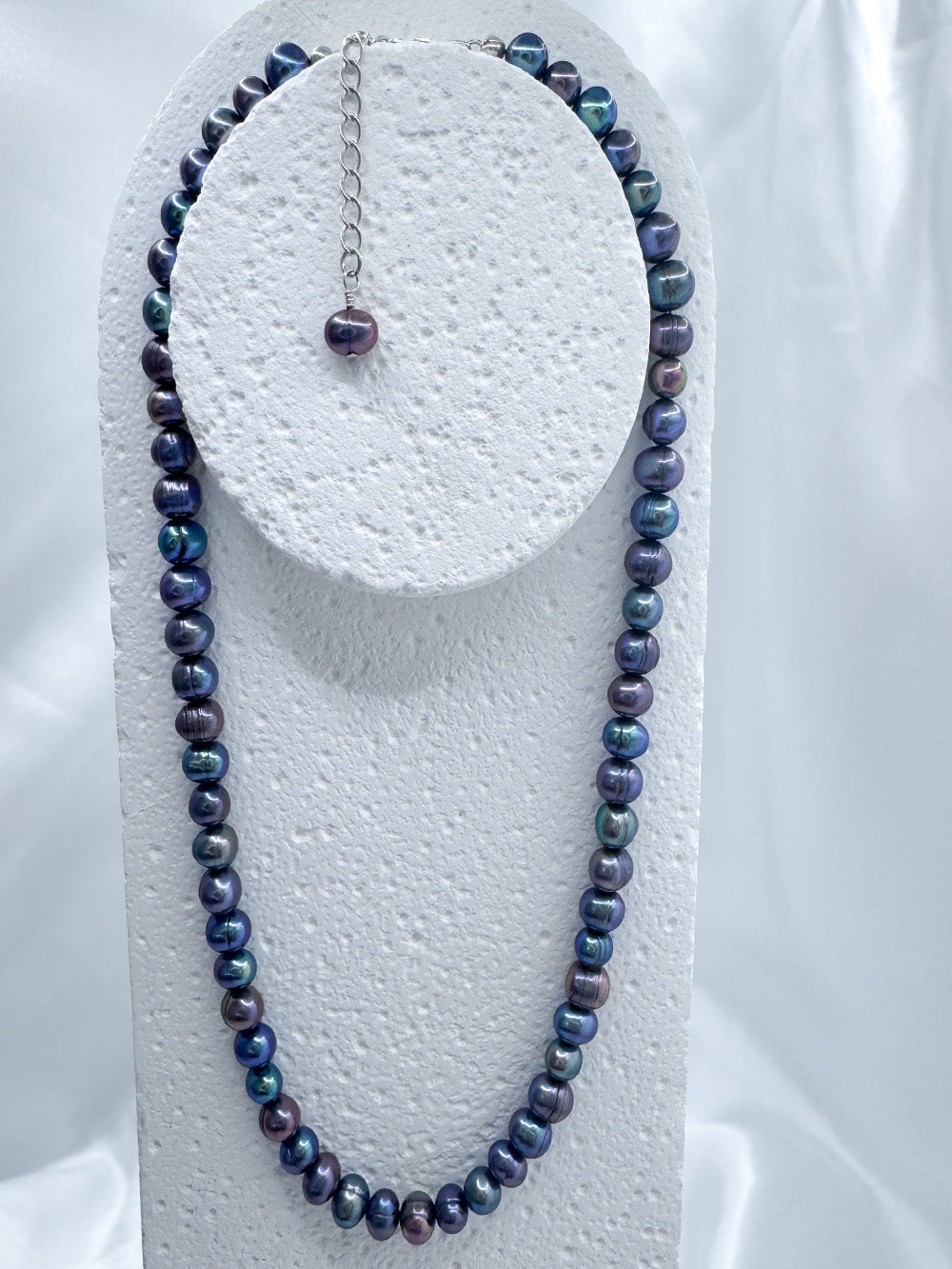 Full view of iridian's metallic blue pearl and sterling silver fully beaded necklace on a white display
