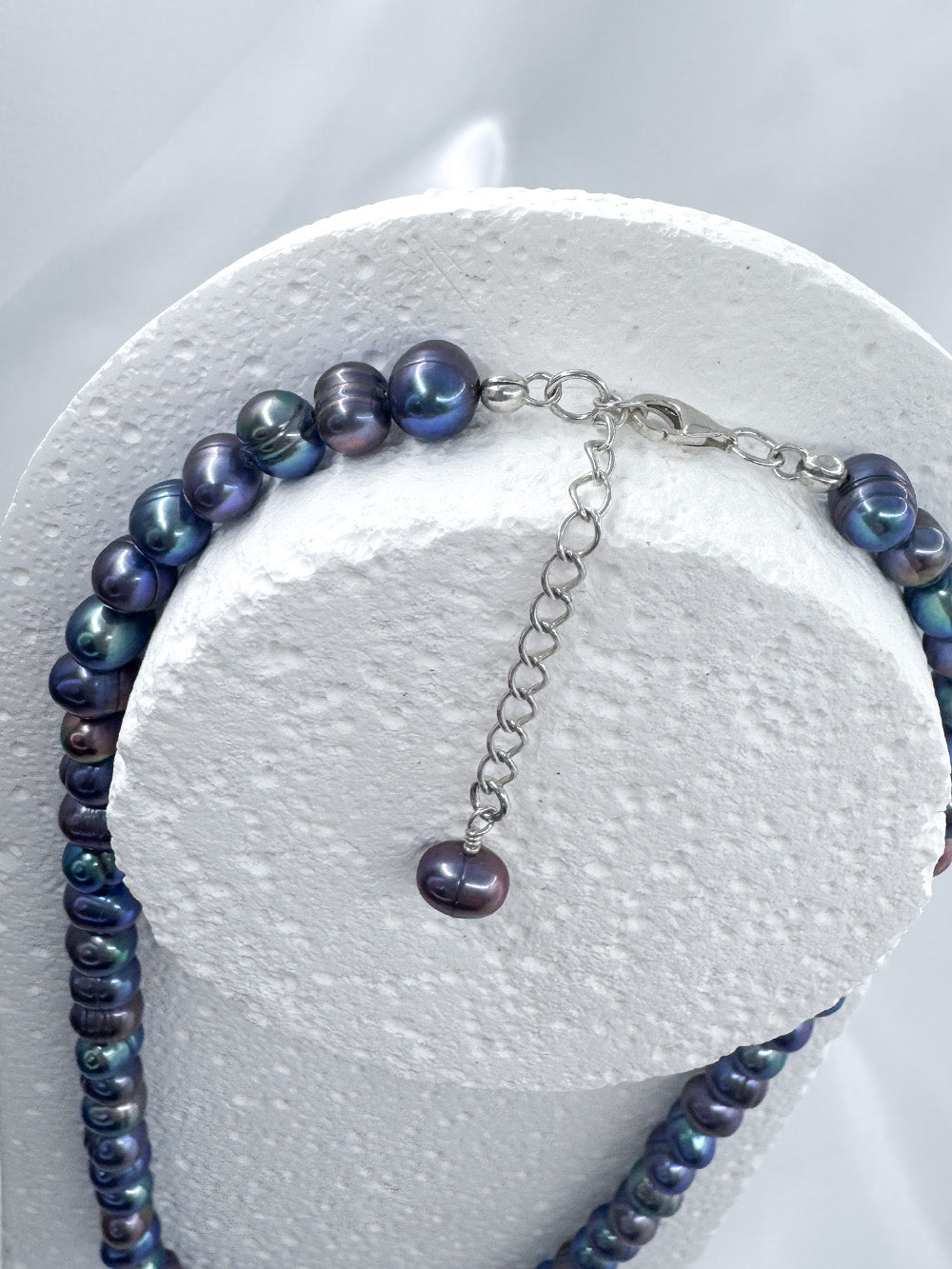 Close up on clasp and extender chain on iridian's metallic blue pearl and sterling silver fully beaded necklace on a white display
