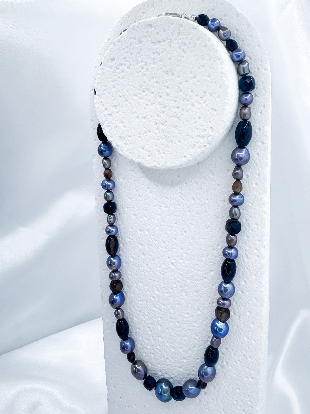 Mid shot of iridian's pearl, agate and sterling silver necklace on a white display bust