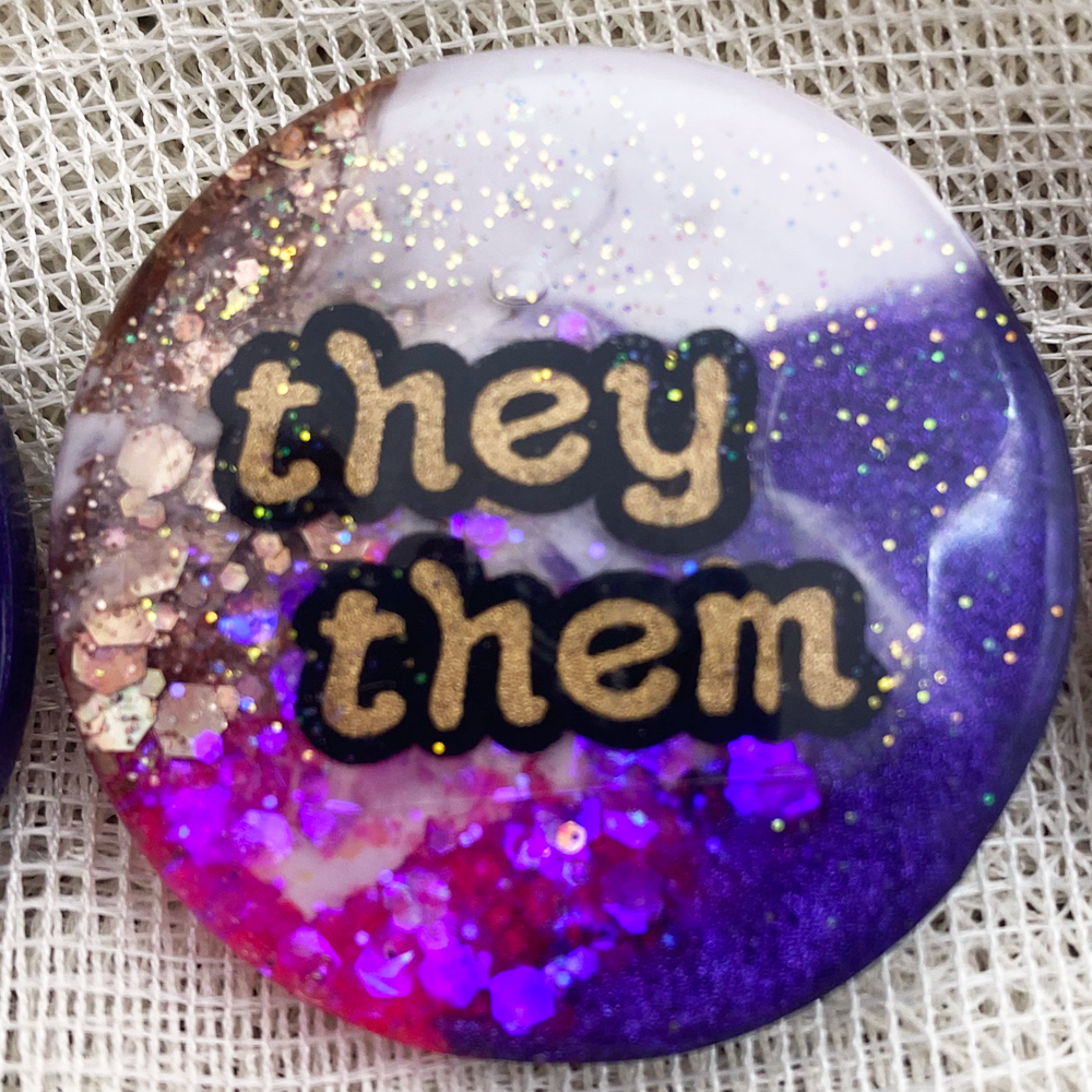 Iridian's purple, pink, white and gold statement pronoun badge with  they/them label