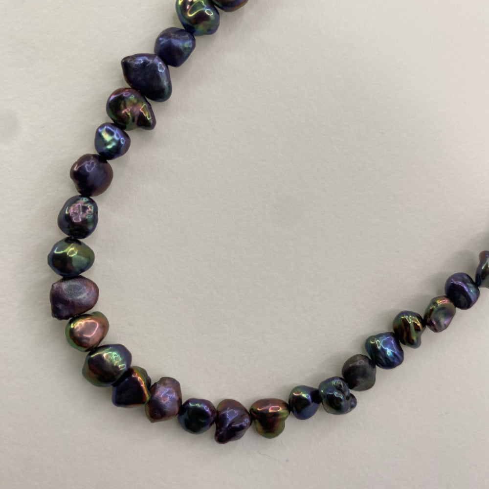Close up of a black rainbow keshi pearl necklace on a white background