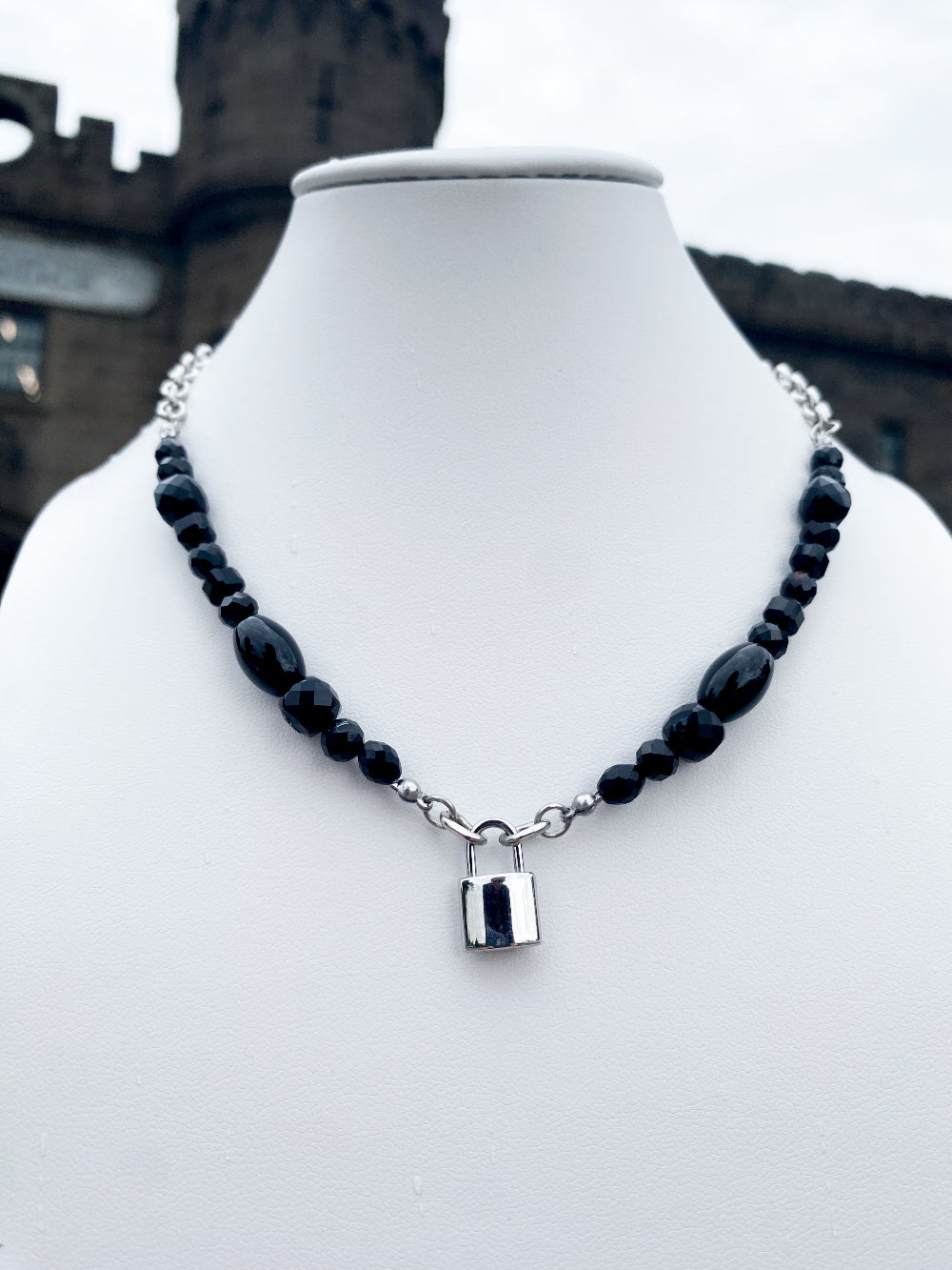 Beadedc black agate and lock pendant necklace on a white bust in a moody setting 