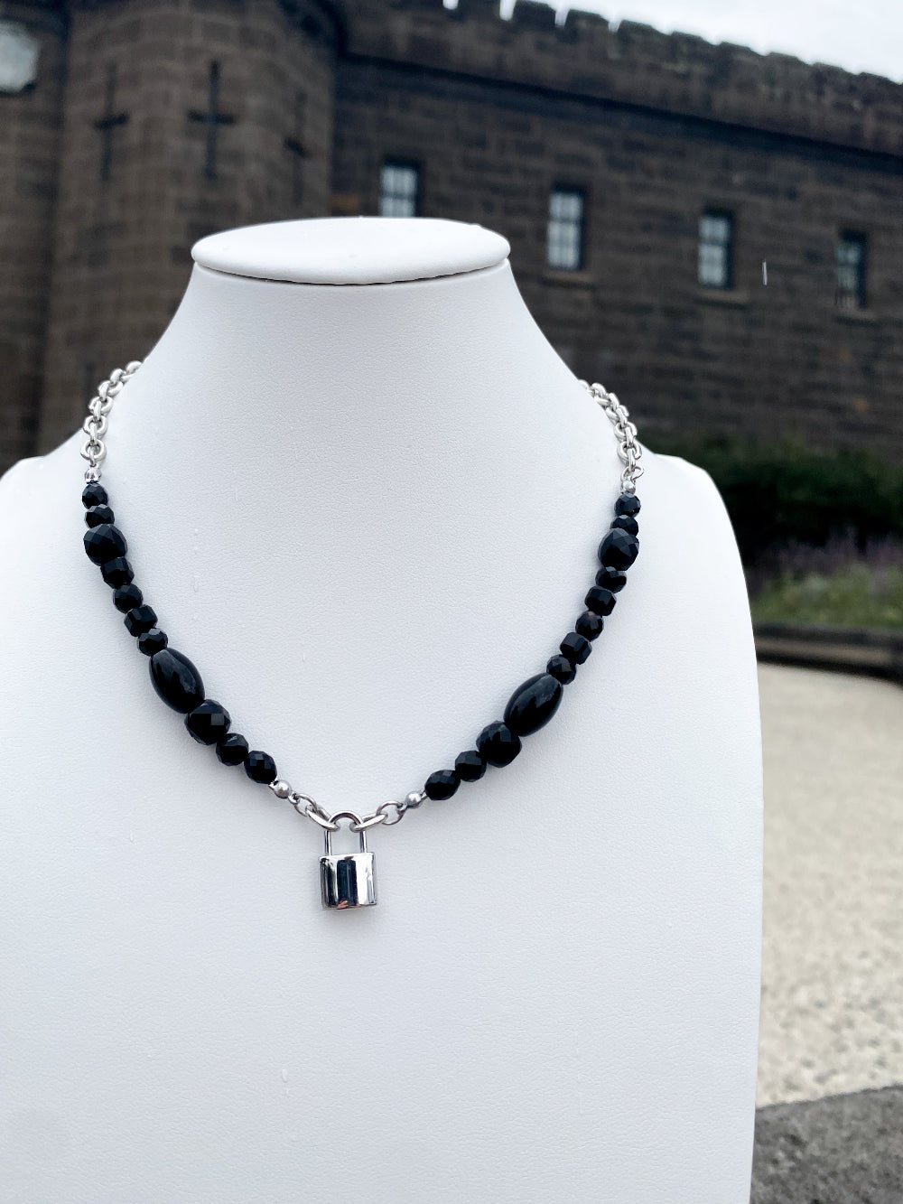 Beaded agate and lock pendant steel necklace on white bust with bricks in background