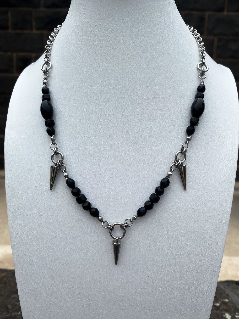 A necklace with black agate beaded asegments and spike charms onb a white bust