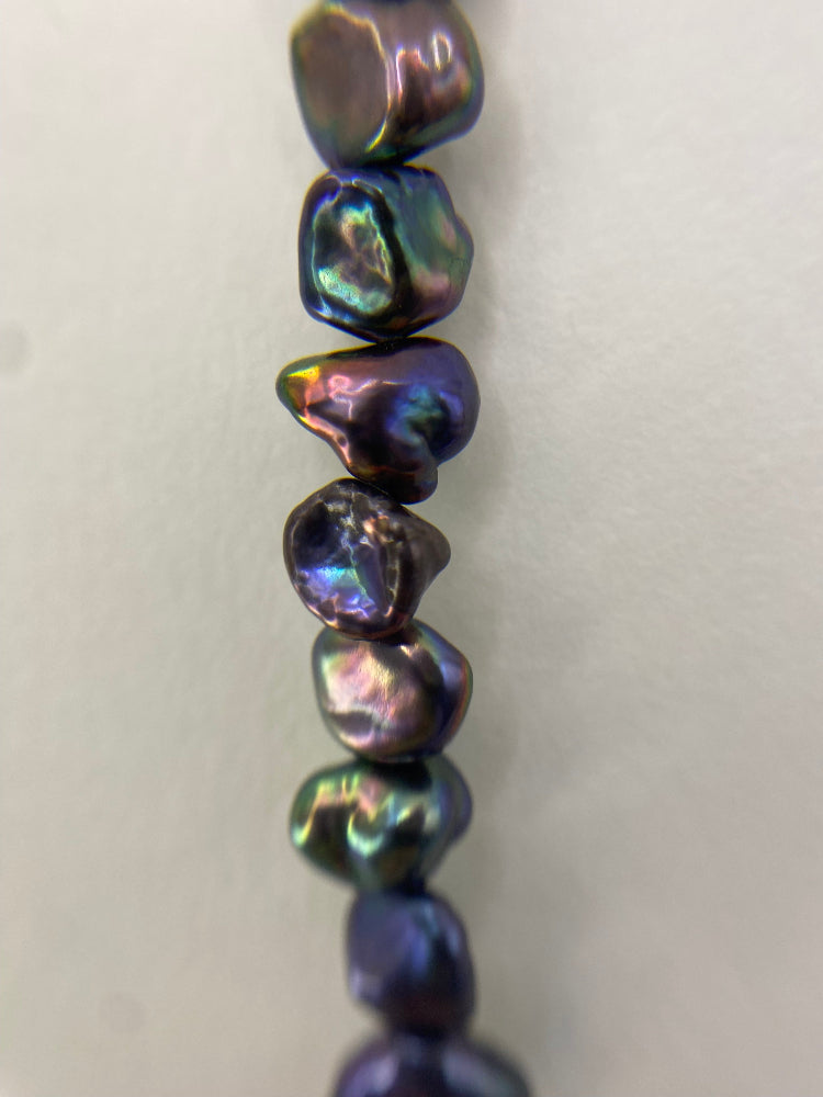 Close up of black rainbow keshi pearls on a white background