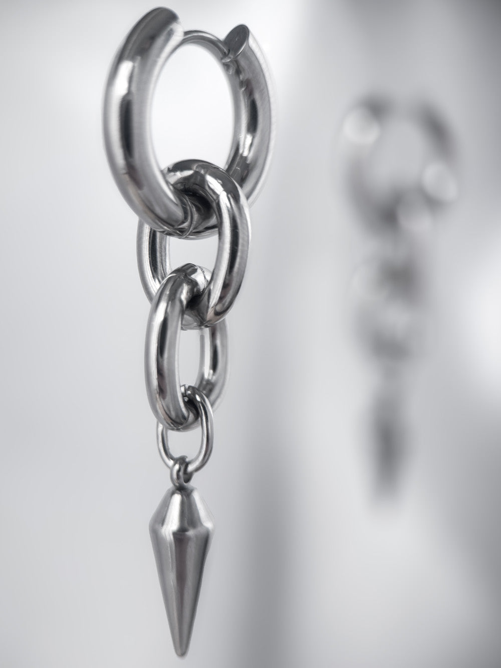 iridian design's 316L stainless steel maxi hoop floating in mid air, a second earring out of focus in the background