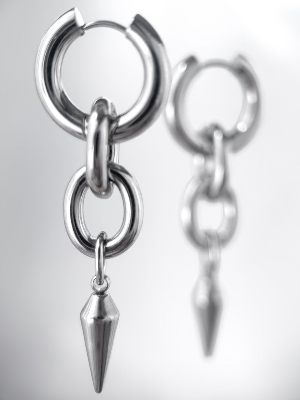 iridian design's 316L stainless steel maxi hoop floating in mid air, a second earring out of focus in the background