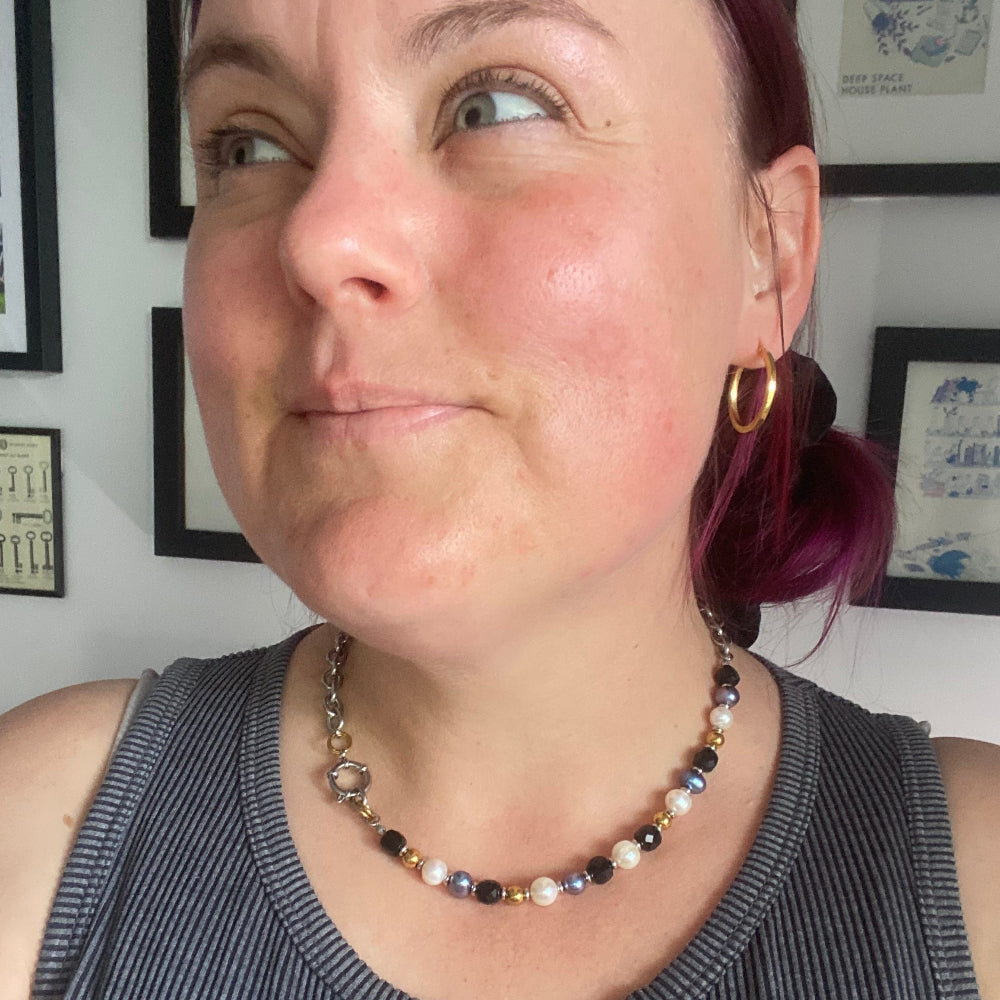 Person wearing a non-binary pride necklace with pearls and semi-precious stones