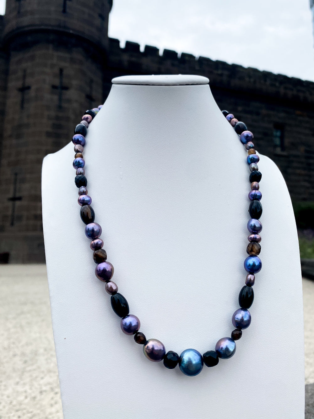Beaded vibrant pearl and black agate necklace on white bust with bricks in background