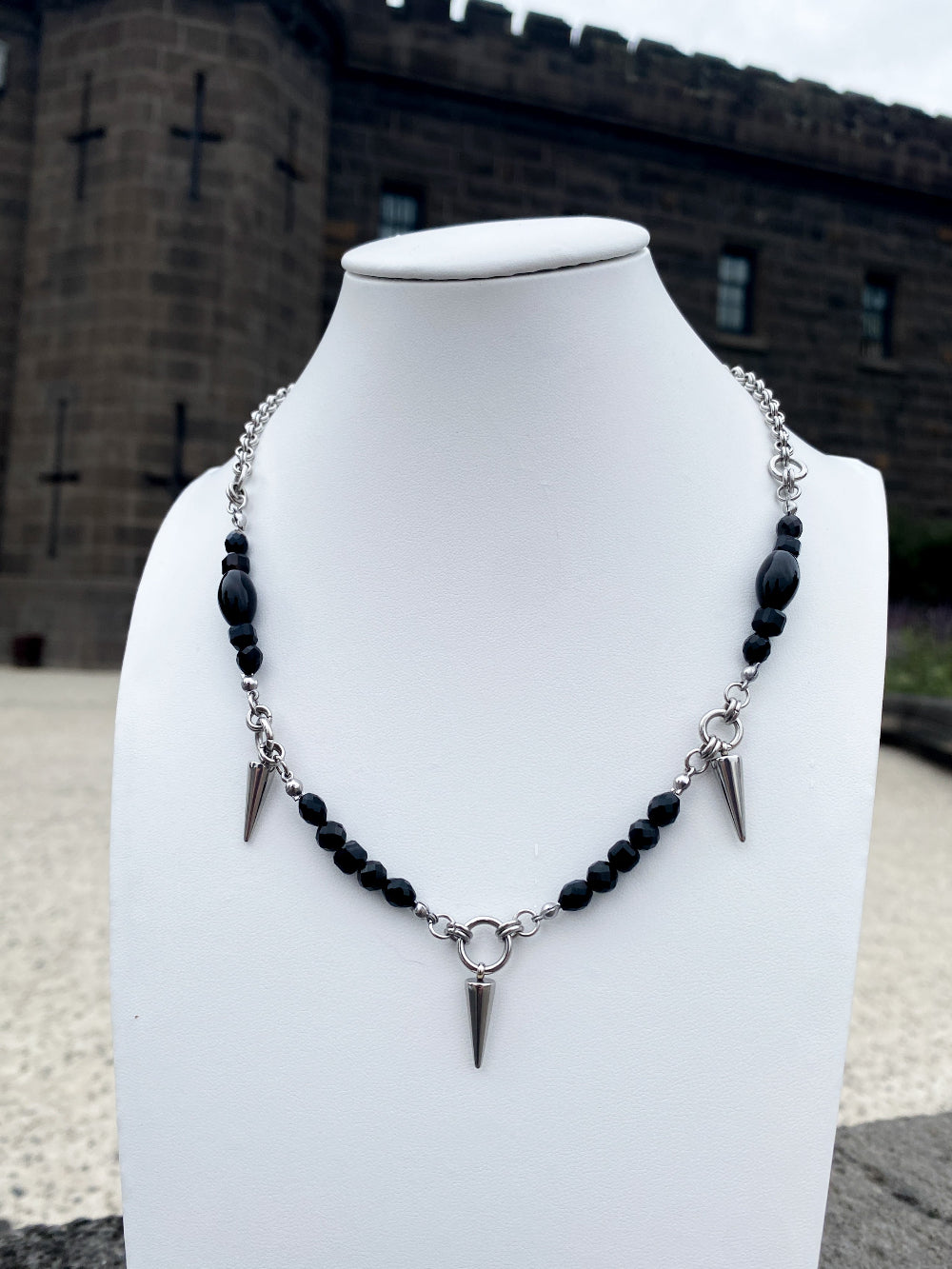 Beaded necklace with steel spike charms on white bust with bricks in background