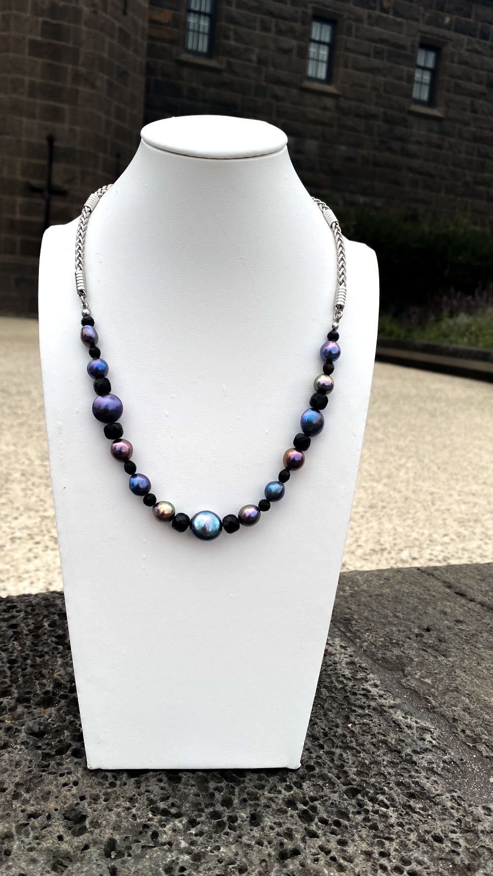 A rainbow pearl and black agate necklace on a white bust in a moody setting