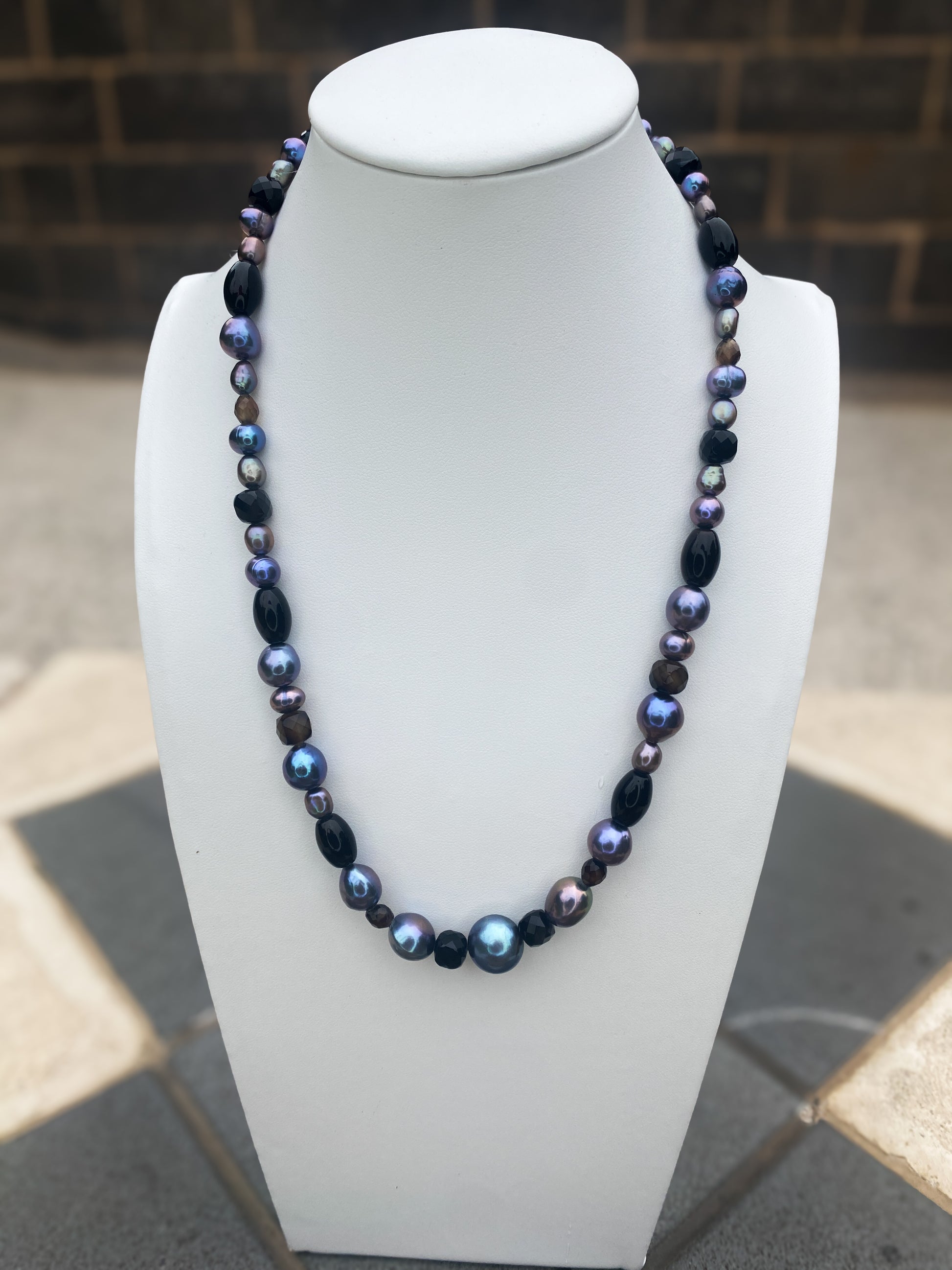 Beaded pearl, agate and silver necklace on a white bust in an. urban setting